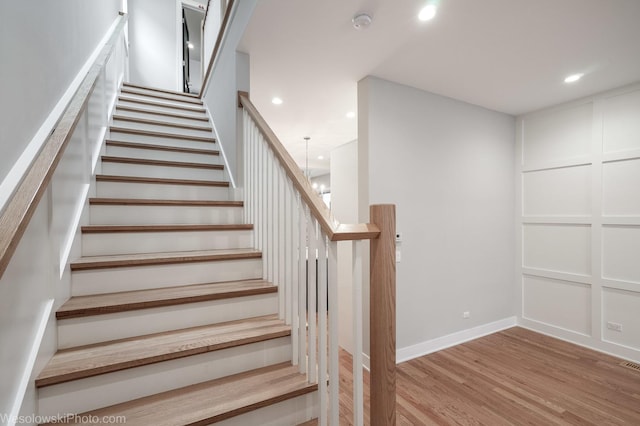 staircase with wood-type flooring and an inviting chandelier