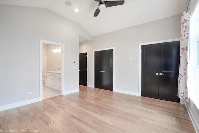 unfurnished bedroom featuring lofted ceiling, light hardwood / wood-style flooring, ceiling fan, connected bathroom, and multiple closets