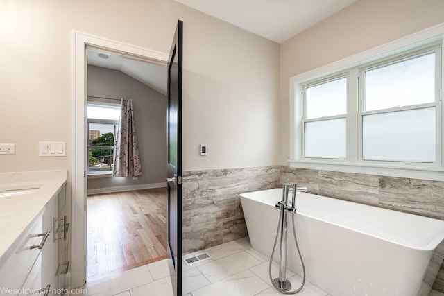 bathroom featuring vanity, a bathtub, lofted ceiling, and tile walls