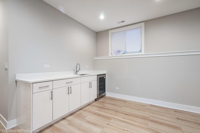 interior space featuring wine cooler, white cabinetry, sink, and light hardwood / wood-style flooring