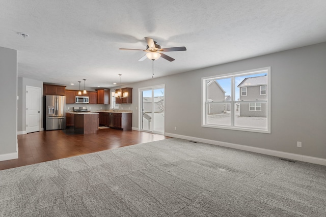 unfurnished living room featuring a textured ceiling, dark carpet, and ceiling fan with notable chandelier