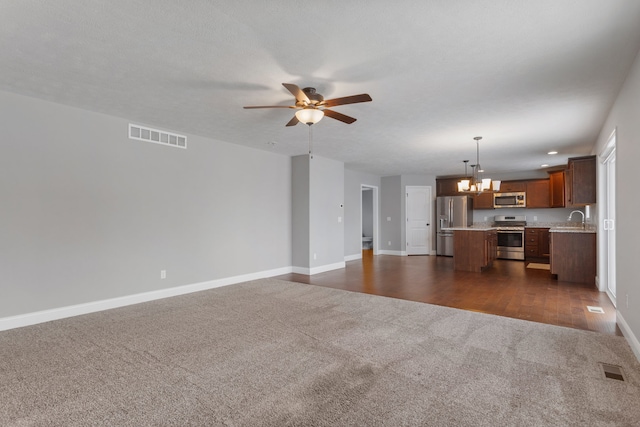 unfurnished living room featuring a textured ceiling, sink, dark carpet, and ceiling fan with notable chandelier