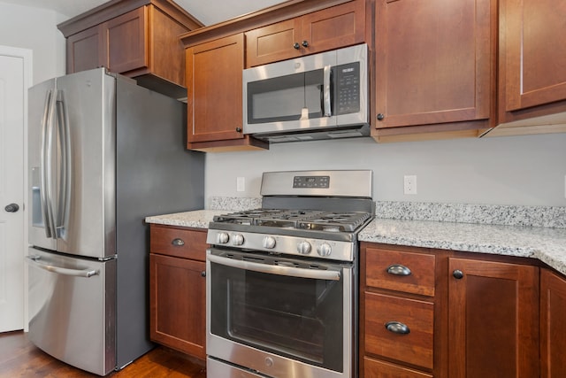 kitchen with stainless steel appliances, light stone counters, and dark hardwood / wood-style floors