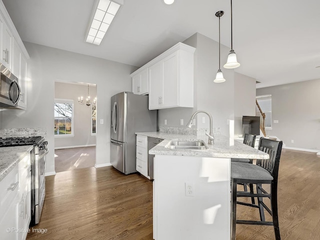 kitchen with a kitchen bar, appliances with stainless steel finishes, sink, pendant lighting, and white cabinetry