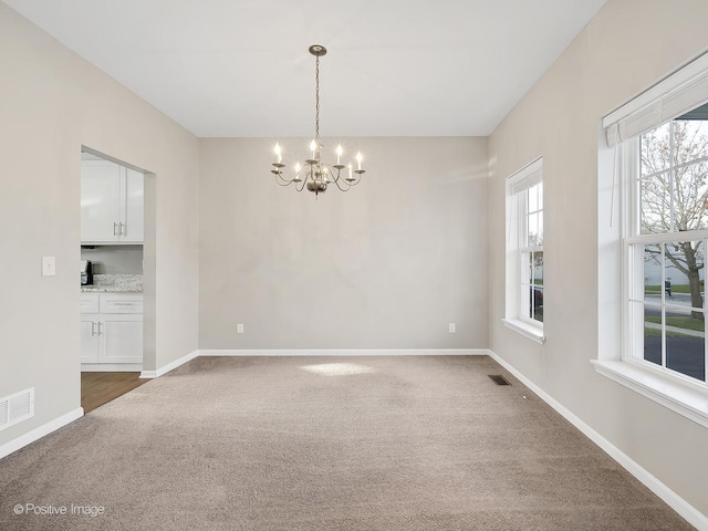 carpeted empty room with a chandelier and a wealth of natural light