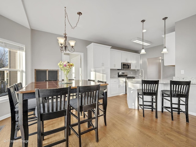 dining space featuring light wood-type flooring, a notable chandelier, and sink