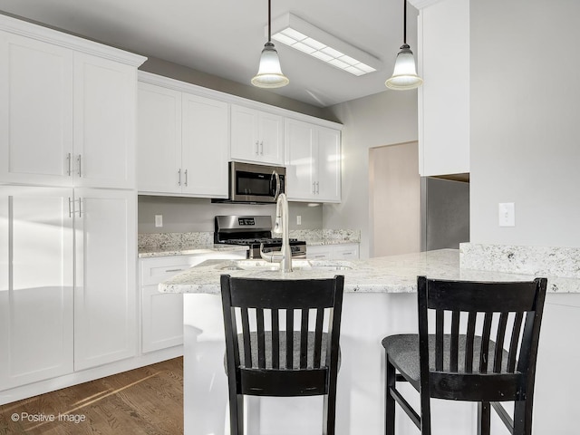 kitchen featuring white cabinets, stainless steel appliances, light stone countertops, and a breakfast bar area