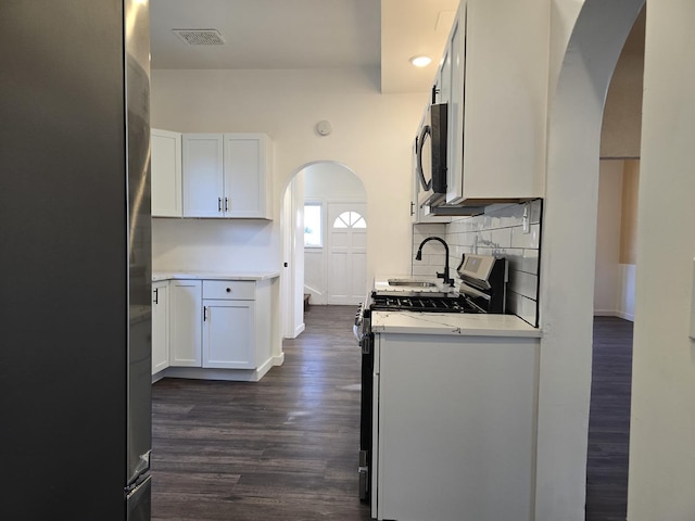 kitchen featuring decorative backsplash, gas range oven, white cabinetry, and stainless steel refrigerator