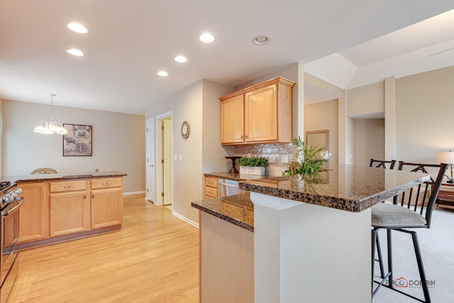 kitchen with dark stone counters, an inviting chandelier, light wood-type flooring, appliances with stainless steel finishes, and a breakfast bar area