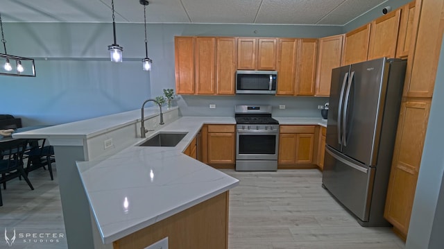 kitchen featuring kitchen peninsula, appliances with stainless steel finishes, light stone countertops, sink, and pendant lighting