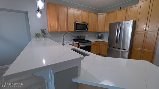 kitchen with kitchen peninsula, appliances with stainless steel finishes, a kitchen bar, light stone counters, and hanging light fixtures