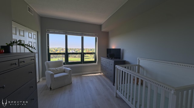 bedroom with a textured ceiling, light hardwood / wood-style floors, and a crib