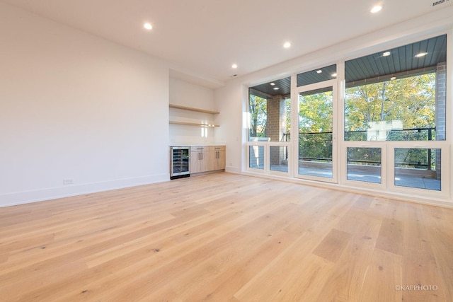 unfurnished living room featuring light hardwood / wood-style flooring, beverage cooler, and indoor bar