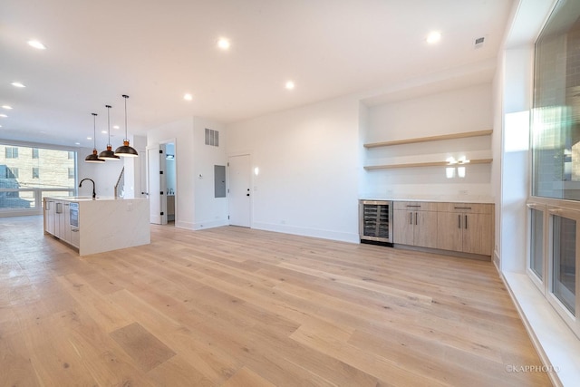 unfurnished living room with light wood-type flooring, electric panel, beverage cooler, and sink