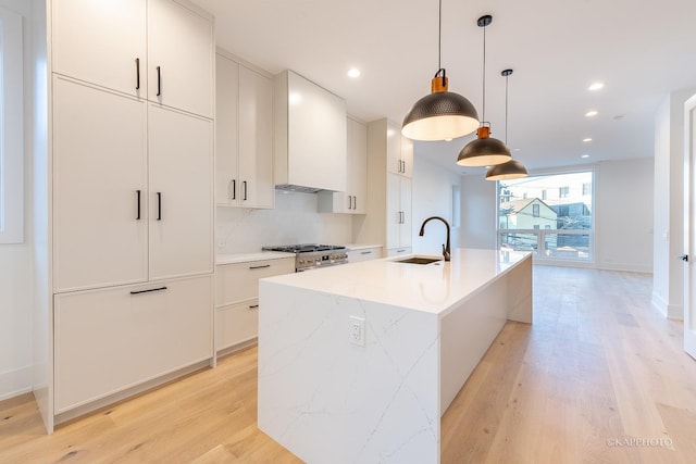 kitchen with premium range hood, a kitchen island with sink, sink, pendant lighting, and white cabinetry