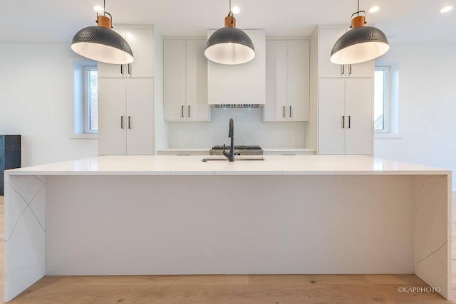 kitchen featuring pendant lighting, white cabinets, and a kitchen island with sink