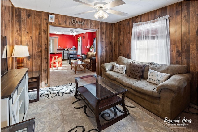 carpeted living room featuring ceiling fan and wooden walls