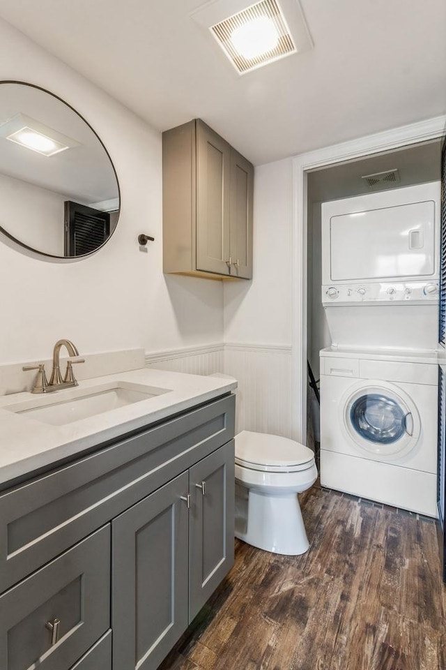 bathroom featuring stacked washer / dryer, toilet, vanity, and hardwood / wood-style flooring