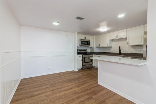 kitchen with white cabinetry, sink, stainless steel appliances, hardwood / wood-style floors, and decorative backsplash