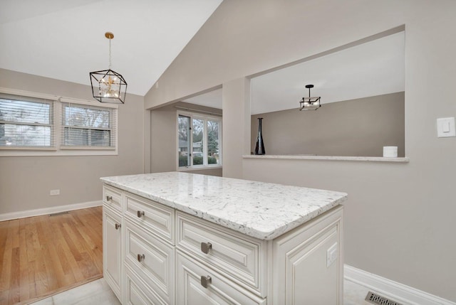 kitchen with vaulted ceiling, decorative light fixtures, white cabinetry, light stone counters, and light wood-type flooring