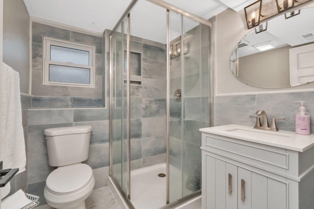 bathroom with vanity, toilet, a shower with shower door, and tile walls