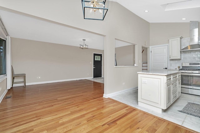 kitchen with wall chimney range hood, stainless steel gas range, white cabinetry, a notable chandelier, and decorative backsplash