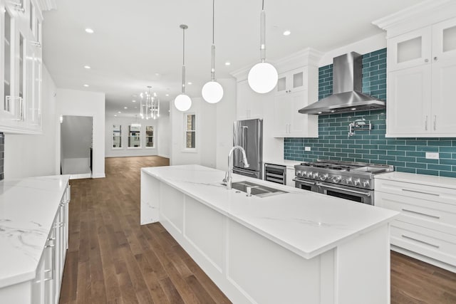 kitchen with white cabinetry, premium appliances, a center island with sink, hanging light fixtures, and wall chimney range hood