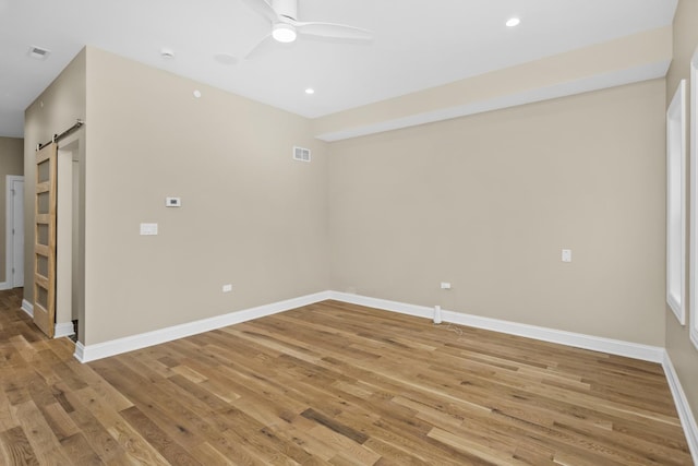 spare room featuring ceiling fan, a barn door, and wood-type flooring