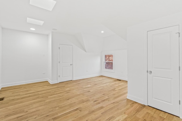 bonus room with light wood-type flooring and vaulted ceiling with skylight