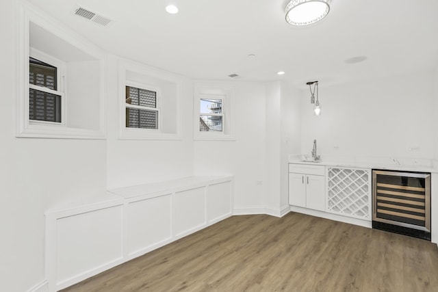 bar with sink, white cabinetry, hanging light fixtures, light wood-type flooring, and beverage cooler