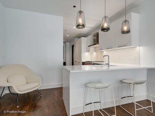 kitchen featuring decorative backsplash, wall chimney range hood, white cabinets, and kitchen peninsula