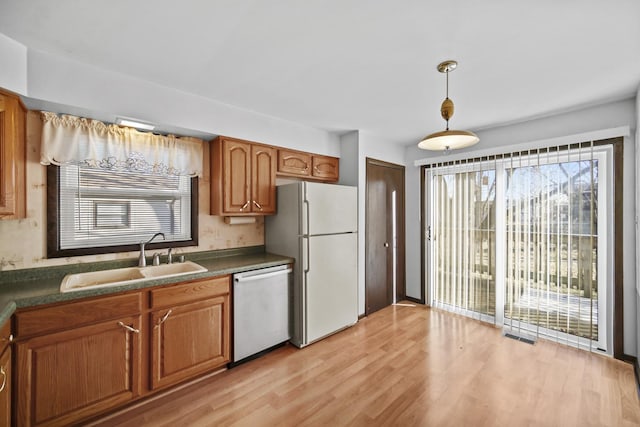 kitchen with white appliances, light hardwood / wood-style floors, hanging light fixtures, and sink