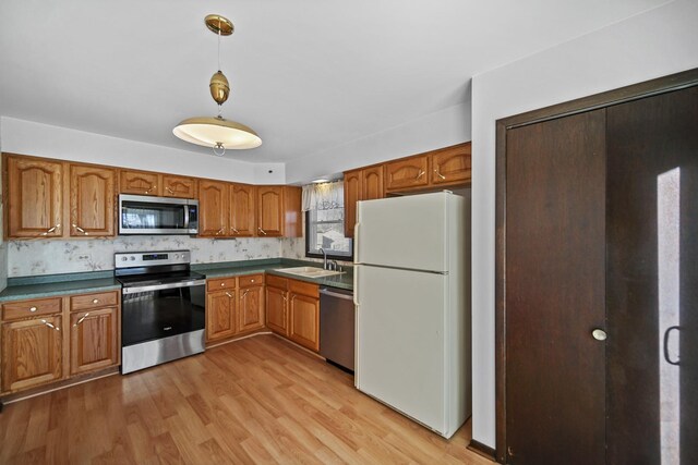 kitchen featuring sink, hanging light fixtures, stainless steel appliances, backsplash, and light wood-type flooring