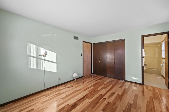 unfurnished bedroom featuring a closet, light wood-type flooring, and ensuite bath