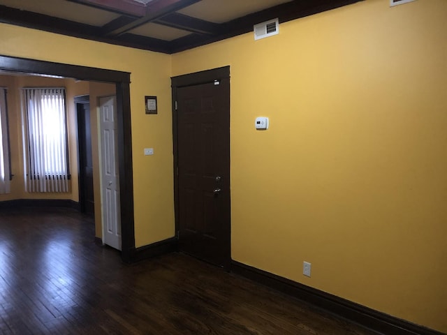 empty room featuring beam ceiling, dark wood-type flooring, and coffered ceiling