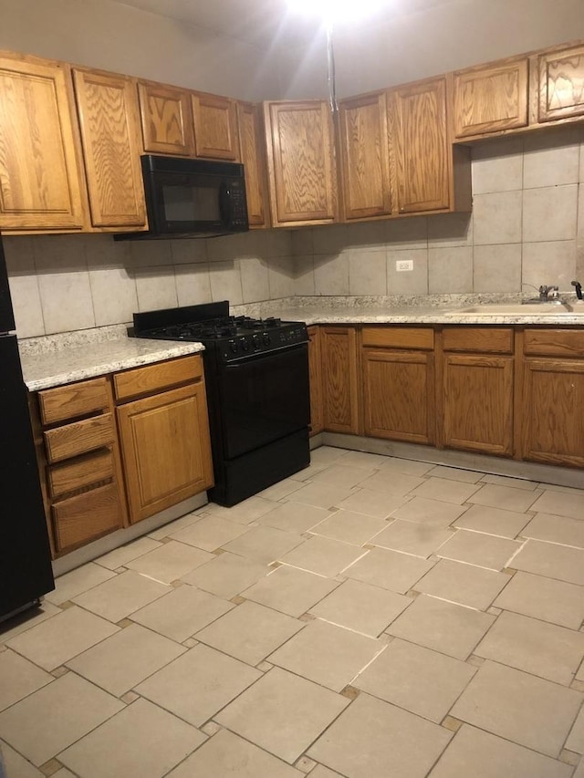 kitchen with black appliances, sink, light stone countertops, and backsplash