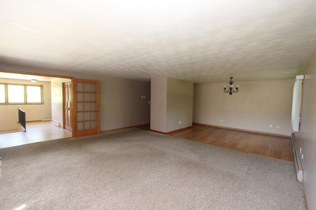 spare room featuring a baseboard heating unit, a textured ceiling, light colored carpet, and a notable chandelier