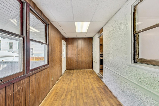 corridor featuring a paneled ceiling, light hardwood / wood-style flooring, and wooden walls