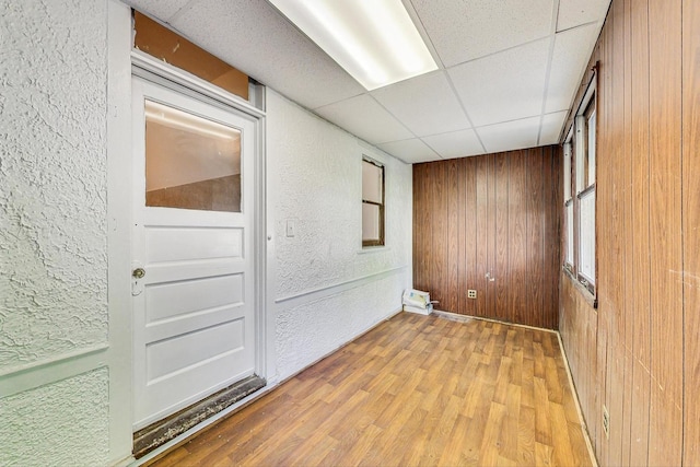 empty room featuring hardwood / wood-style floors, a drop ceiling, and wooden walls