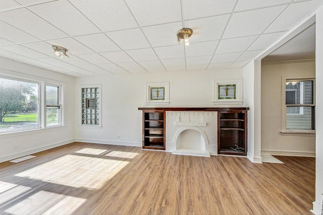 unfurnished living room with wood-type flooring, a paneled ceiling, and a brick fireplace