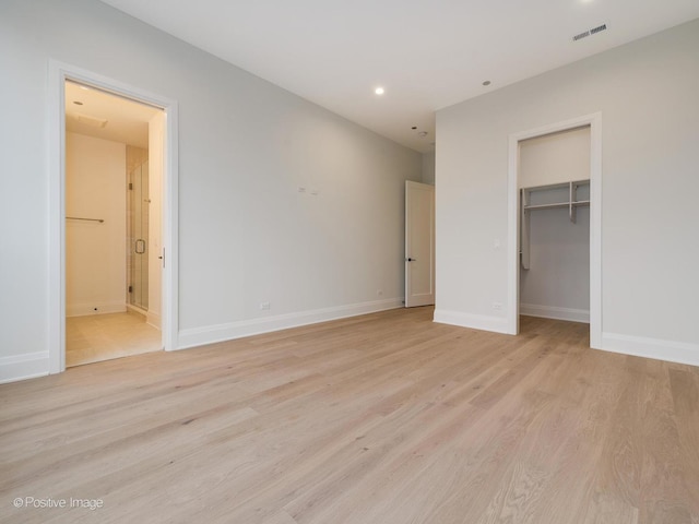 unfurnished bedroom featuring a walk in closet, light hardwood / wood-style floors, ensuite bath, and a closet