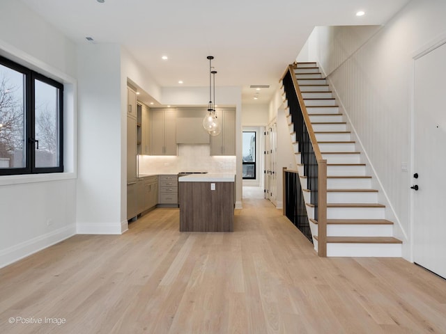 kitchen featuring backsplash, gray cabinetry, light hardwood / wood-style flooring, a kitchen island, and hanging light fixtures