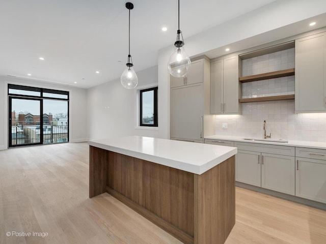 kitchen featuring a center island, sink, decorative backsplash, decorative light fixtures, and light hardwood / wood-style floors