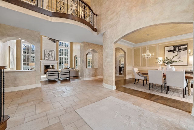 foyer featuring a high ceiling, a large fireplace, an inviting chandelier, and ornamental molding