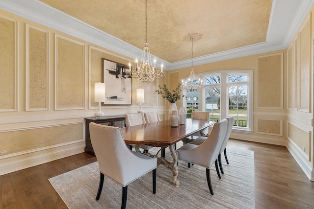 dining space with crown molding, dark wood-type flooring, a tray ceiling, and a chandelier