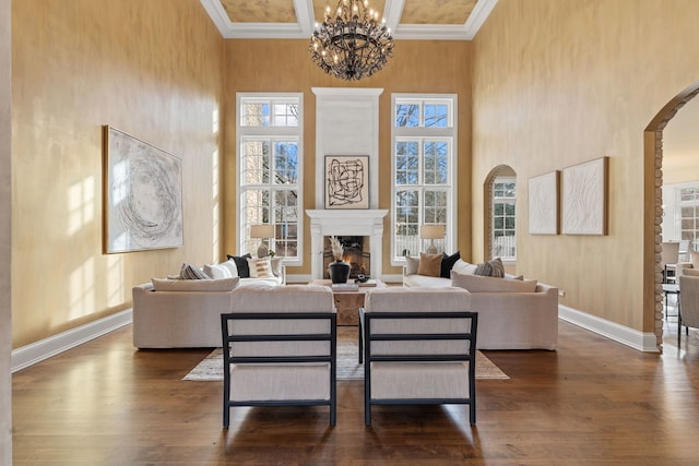 living room featuring dark hardwood / wood-style flooring, a towering ceiling, ornamental molding, coffered ceiling, and an inviting chandelier