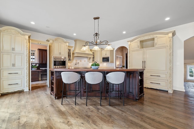 kitchen featuring pendant lighting, decorative backsplash, a center island with sink, and cream cabinets