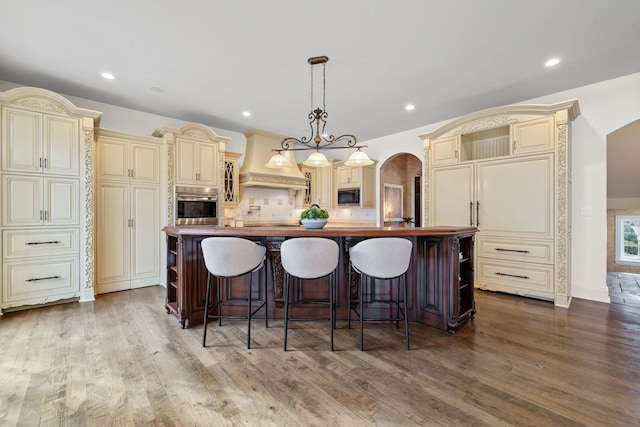 kitchen with built in microwave, a kitchen island with sink, pendant lighting, cream cabinetry, and butcher block counters