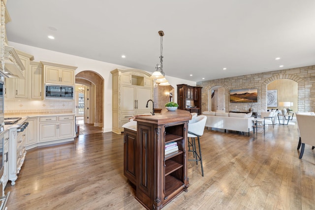 kitchen featuring pendant lighting, cream cabinets, built in microwave, an island with sink, and light hardwood / wood-style floors