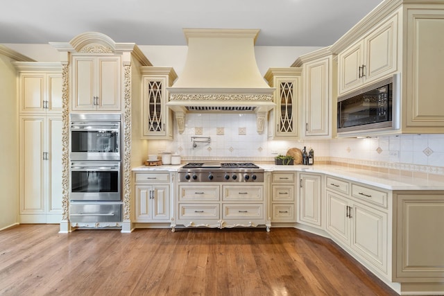 kitchen with custom range hood, black microwave, double oven, stainless steel gas cooktop, and cream cabinets